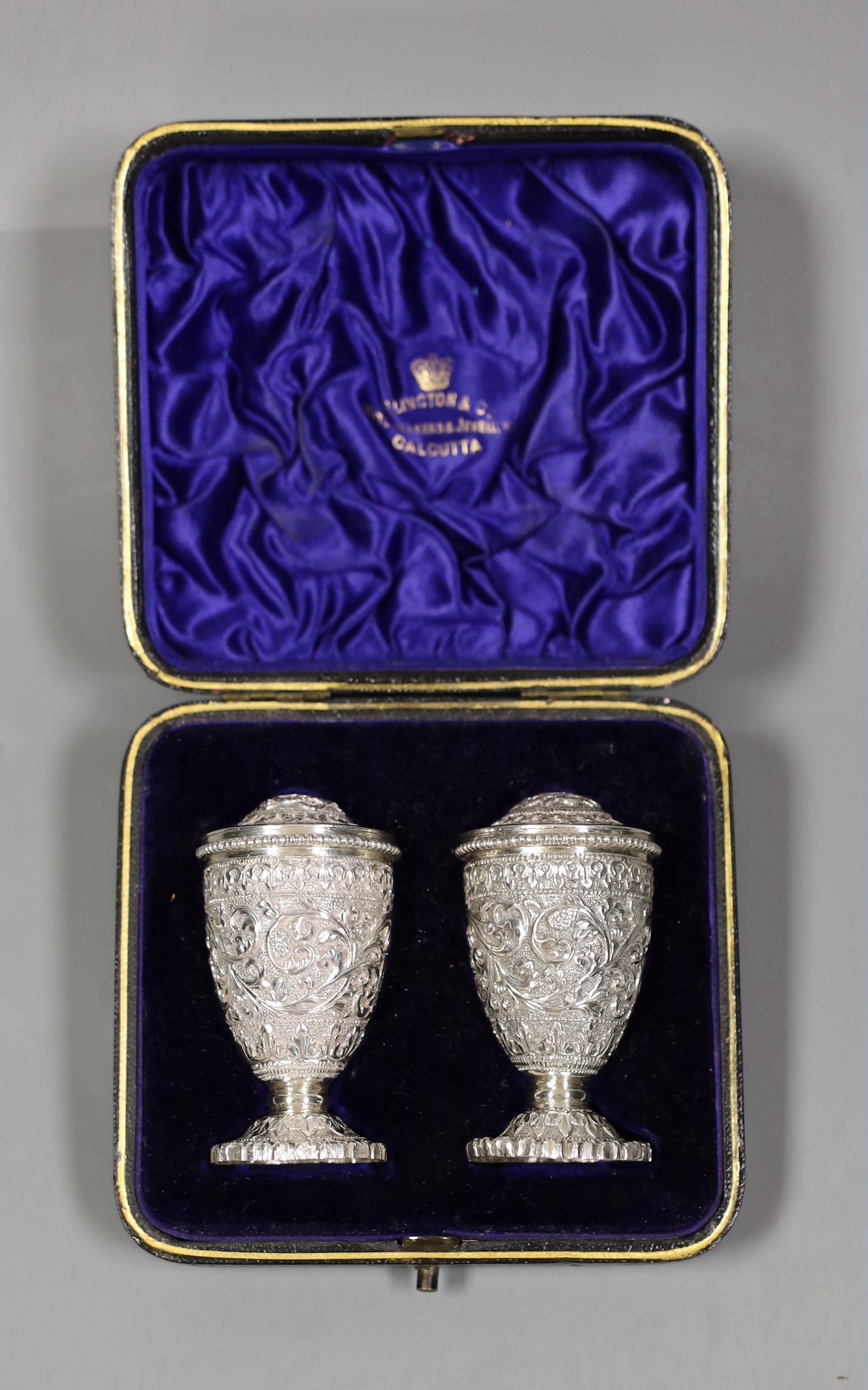 A pair of early 20th century Indian embossed white metal pedestal pepperettes, 7cm, 112 grams, in Elkington & Co, Calcutta, fitted box.